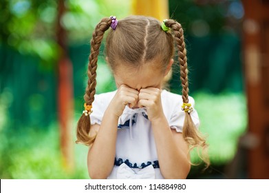 Beautiful little girl with pigtails crying, against background of summer park.