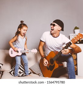 Beautiful Little Girl Playing Guitar With Her Father. Funny Lifestyle Picture. Happy Family Timespending. Girl Holding Pink Ukulele Ang Singing And Jumping,