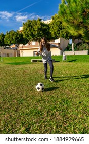 Beautiful Little Girl Playing Soccer On The Grass, Wears A Mask To Protect Herself From The Coronavirus While Doing Sports In A Beautiful Park With Natural Grass. Healthy Life Concept