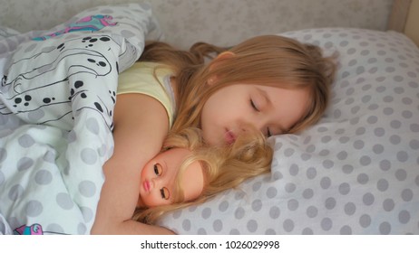 beautiful little girl sleep in a bed and hug her baby doll