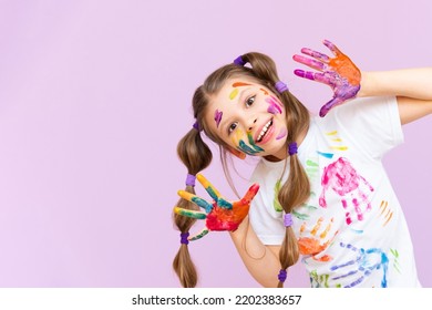 A beautiful little girl stained in multicolored paints on a pink isolated background has fun smiling.
