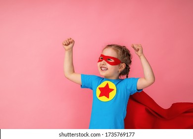 beautiful little girl in a superhero costume, in a red Cape and mask shows how strong she is, isolated against a pink background. Cute kid playing superhero. The concept of Power girl. - Shutterstock ID 1735769177