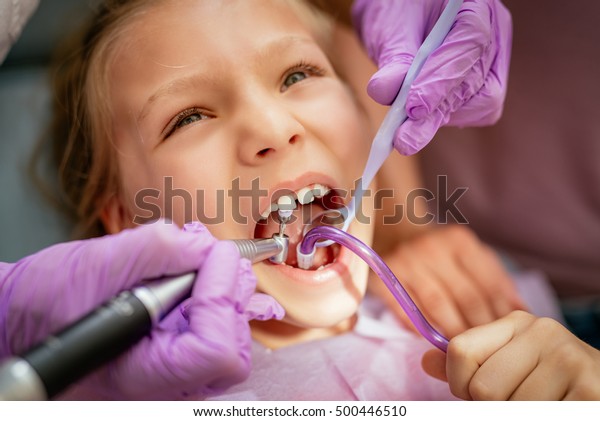 Beautiful little\
girl at visit in the dentist office. She is sitting on a chair and\
dentist polished teeth on\
her.