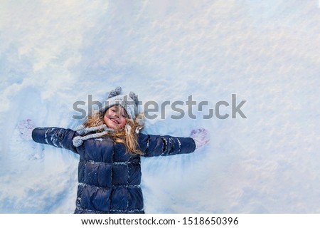 Beautiful little girl wearing navy jacket and knitted hat playing in a snowy winter park. Child playing with snow in winter. Kid play and jump in snowy forest. Family vacation with child in mountains