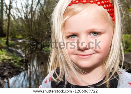 A beautiful little girl wearing a red headband and pretty star dress smiling and looking into the camera, pretty green eyes