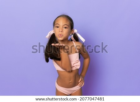 Beautiful little girl wearing swimwear sending air kiss isolated over purple background.