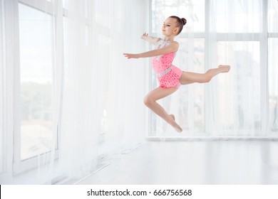 Beautiful little gymnast girl in pink sportswear dress, performing art gymnastics element, jumping, doing split leap in the air. Sport, training, stretching, active lifestyle concept - Powered by Shutterstock