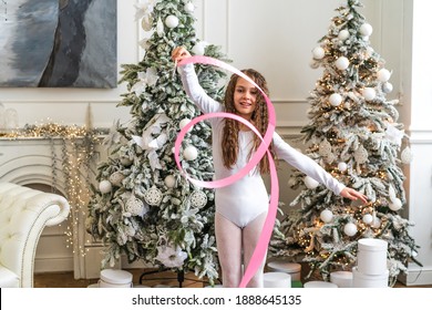 A Beautiful Little Gymnast In A White Sports Dress Doing Rhythmic Gymnastics Exercises Spirals With An Artistic Ribbon In A Fitness Class During The Christmas Season. Sports, Training, Stretching