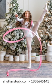 A Beautiful Little Gymnast In A White Sports Dress Doing Rhythmic Gymnastics Exercises Spirals With An Artistic Ribbon In A Fitness Class During The Christmas Season. Sports, Training, Stretching