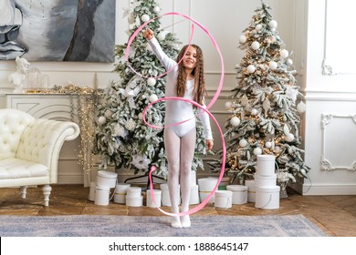 A Beautiful Little Gymnast In A White Sports Dress Doing Rhythmic Gymnastics Exercises Spirals With An Artistic Ribbon In A Fitness Class During The Christmas Season. Sports, Training, Stretching