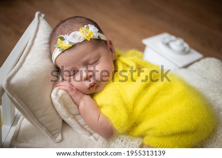 Beautiful little infant baby girl, has happy sleep face, dressed in yellow suit and headband with flowers. Child close up portrait. Lifestyle instagram newborn concept. Amazing kids.