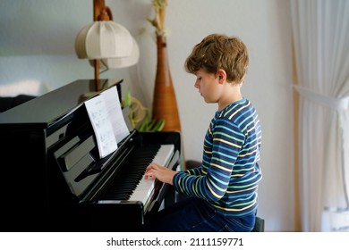 Beautiful little kid boy playing piano in living room. Child having fun with learning to play music instrument with tablet app. E-learning concept during homeschooling corona virus lockdown.