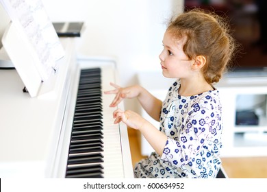 Beautiful Little Kid Girl Playing Piano In Living Room Or Music School. Preschool Child Having Fun With Learning To Play Music Instrument. Education, Skills Concept.