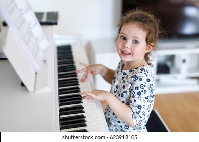 Beautiful Little Kid Girl Playing Piano In Living Room Or Music School. Preschool Child Having Fun With Learning To Play Music Instrument. Education, Skills Concept.