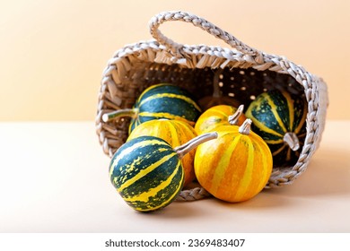 Beautiful little striped pumpkins spilling out of wicker basket close up on beige background with copy space. Halloween. Locally grown - Powered by Shutterstock