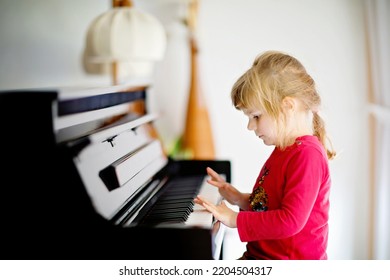 Beautiful Little Toddler Girl Playing Piano In Living Room. Cute Preschool Child Having Fun With Learning To Play Music Instrument. Early Musical Education For Children.