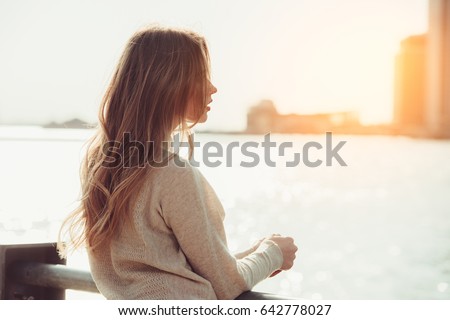 Beautiful lonely girl dreaming and thinking while waiting for date in the city ocean pier at sunset time.