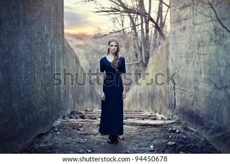 beautiful lonely girl  in long dress near gloomy tunnel on sunset