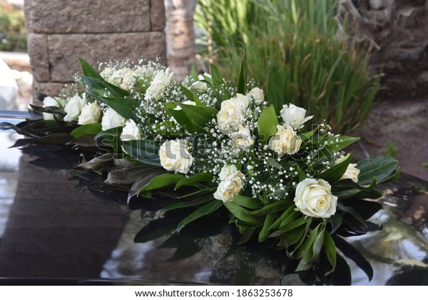 beautiful long bouquet of\
live white roses with green leaves on a black wedding car of the\
newlyweds