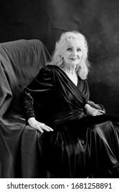 Beautiful Long Grey Haired Senior Woman Sitting On The Chair. Woman Looks Like Old Hollywood  Actress