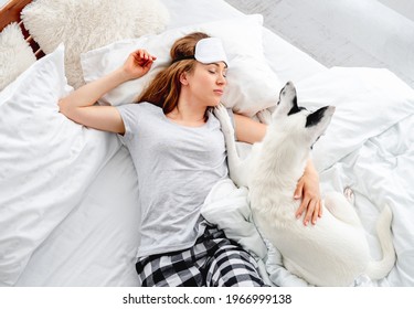 Beautiful Long Hair Girl Lying In The Bed On Her Back With Cute Dog And Sleeping. Pretty Young Woman Resting With Pet. Female Person Wearing Eye Sleeping Mask Napping With Doggy