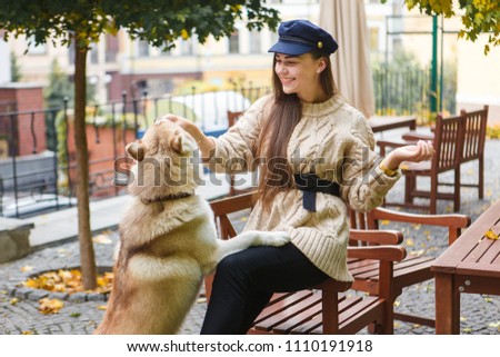 Beautiful long hair women hugging and feeding her husky dog while sitting on the city bench. Playful and happy time spending