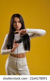 Beautiful Long Haired Woman Holding Black Headphones In Studio. Portrait View Of Attractive Female Dj Looking At Camera, Showing Earphones, Isolated On Orange Background. Concept Of Music.