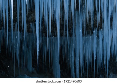 Beautiful long icicles of a frozen waterfall, with water flowing and crashing down and Ice water dripping from the tips of icicles in a cold eery and moody atmosphere in a cave in the mountains