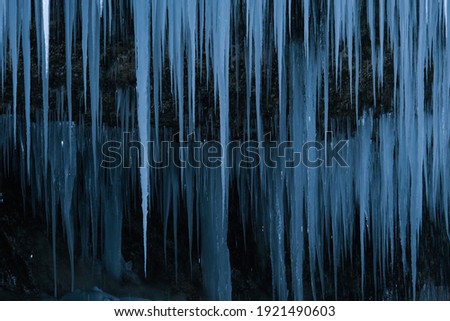 Beautiful long icicles of a frozen waterfall, with water flowing and crashing down and Ice water dripping from the tips of icicles in a cold eery and moody atmosphere in a cave in the mountains