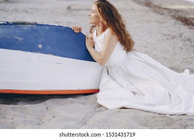 Beautiful long-haired bride in a magnificent white dress sitting near boat