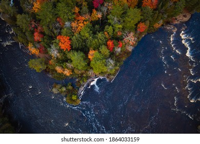 Beautiful look down aerial of a colorful tree covered peninsula and shoreline in autumn along the Tahquamenon River in Upper Michigan with green, red, yellow and orange leaves.