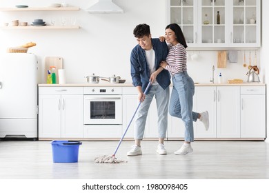 Beautiful loving asian young couple mopping floor in kitchen together, full length photo, copy space. Romantic cheerful chinese lady hugging her smiling boyfriend while cleaning house - Powered by Shutterstock