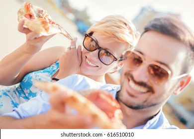 Beautiful loving couple sitting on the bench in the center of the city and eating pizza. Dating, consumerism, food, lifestyle concept