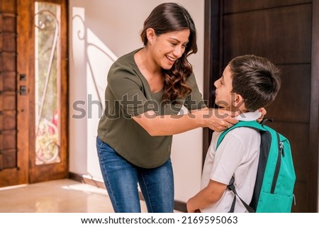 Beautiful loving  Latin mother with her children at the door of her house. Mother greets her children who return from school. Children with uniforms and backpacks.