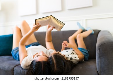 Beautiful Loving Mom And Young Kid Reading Together A Children's Book While Relaxing Together On The Couch