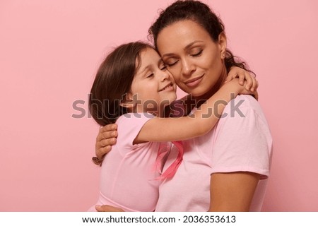 Beautiful loving mother and daughter, hugging each other, wearing pink clothes with a pink ribbon, symbol of World Breast Cancer awareness Day in October. World Cancer Day national Cancer Survivor Day