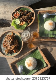 beautiful lunch, two portions of round rice covered in banana leaves, a brown wood serving plate, one portion of grilled chicken and bake crab served on the wooden table