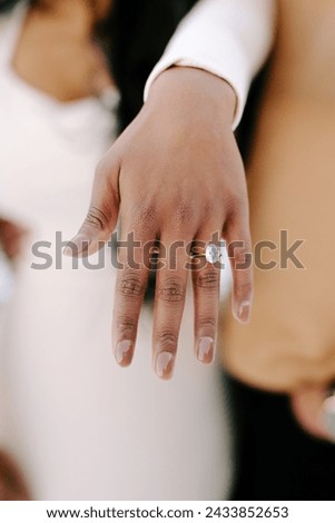 Beautiful luxury oval cut diamond and gold engagement ring showcased on bride to be's hand with brown nails and white dress on cold Colorado day