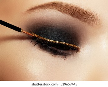 Beautiful macro shot of female eye with ceremonial makeup. Perfect shape of eyebrows, eyeliner and pretty gold line on eyelid. Cosmetics and make-up. Closeup macro shot of fashion sparcle visage