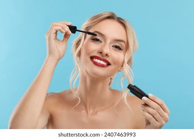 Beautiful makeup. Smiling woman applying mascara on light blue background - Powered by Shutterstock