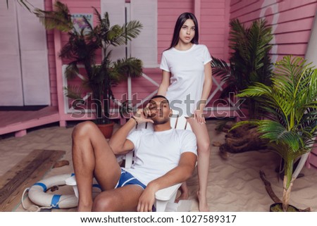 Beautiful man and girl in white T-shirts near the beach house. Mock-up.