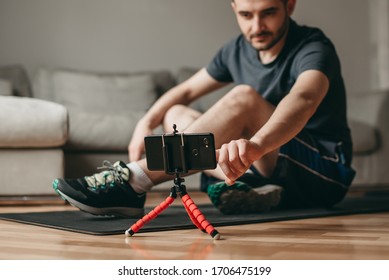 Beautiful Man Watching And Doing  Exercises On A Mat. Sport In Quarantine At Home. Online Lessons. Workout With An Application On A Smartphone.