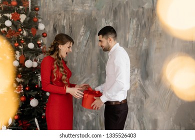 Beautiful man and woman in fancy closes pose before rich decorated Christmas tree and exchange their presents - Shutterstock ID 1335526403