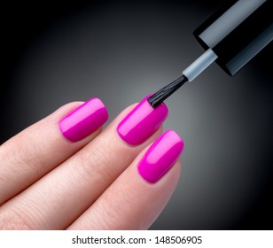 Beautiful manicure process. Nail polish being applied to hand, polish is a pink color. Black background closeup.