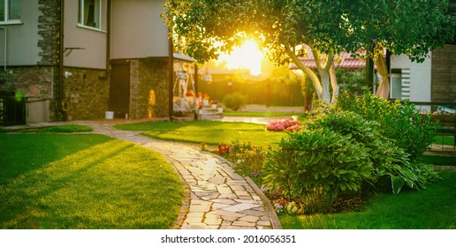 Beautiful manicured lawn and flowerbed with deciduous shrubs on private plot and track to house against backlit bright warm sunset evening light on background. Soft focusing in foreground. - Powered by Shutterstock