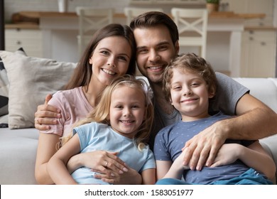 Beautiful Married Couple And Little Pre-school Children Pretty Son And Sweet Daughter Sitting On Couch Looking At Camera Feels Happy. Concept Of Welfare Full Family Portrait, New Home, Capture Moment