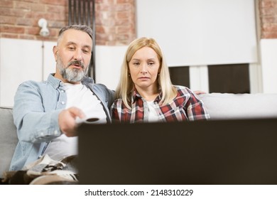 Beautiful Married Couple Of Two Mature People Sitting In Embrace On Comfy Couch And Watching Film On Modern Laptop. Domestic Lifestyles Of Caucasian Family.