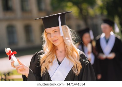 Beautiful master. Beautiful girl holding her rolled diploma with red ribbon in her hand being happy at her graduation ceremony. - Shutterstock ID 1471441334