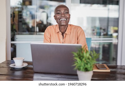 Beautiful mature african woman sitting in a bar outdoor and working with laptop - Black woman looking in camera and smiling - Powered by Shutterstock