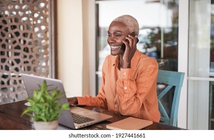 Beautiful mature african woman working with laptop while talking on a call with smartphone  - Powered by Shutterstock